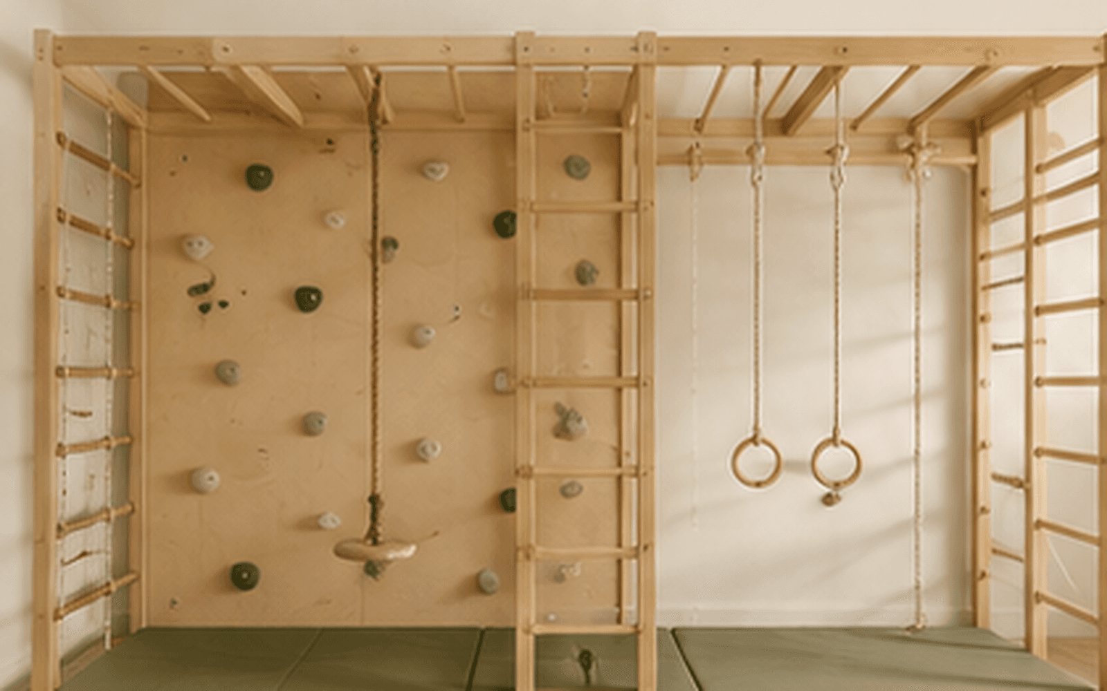 Natural wood movement zone with climbing wall, rings, ladders and soft landing mats in a premium children's playroom.