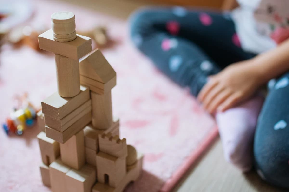 Young child sitting on a soft mat, deeply engaged in creative construction with wooden building blocks