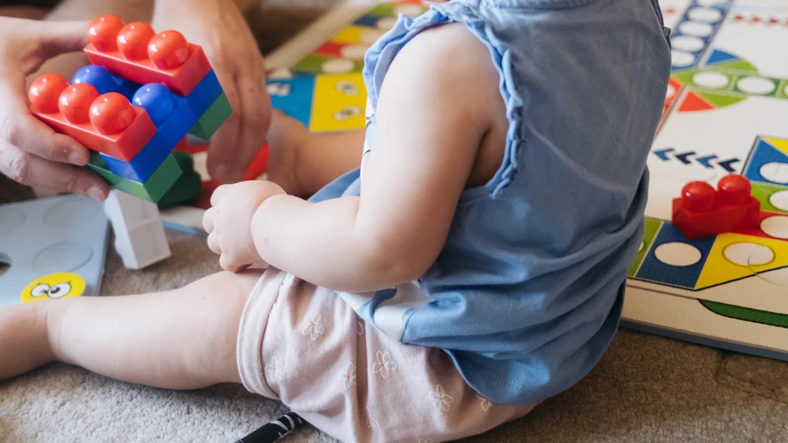 Young child focused on building with blocks on a cozy living room rug with adult in calm proximity